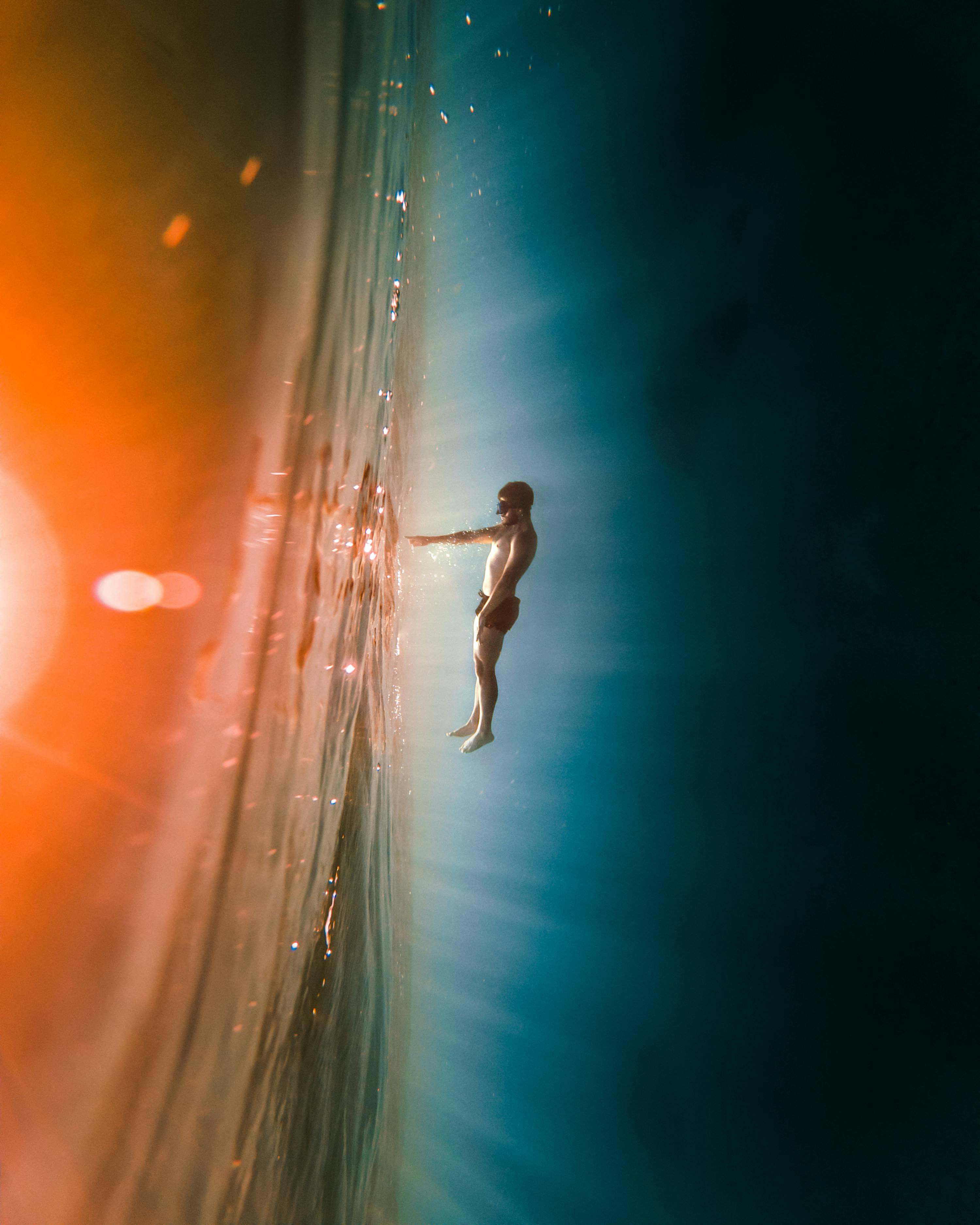 A person floats underwater with sunlight creating vibrant abstract reflections.