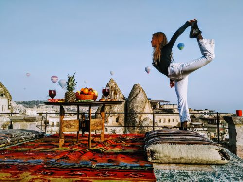 Free Woman performing yoga on a colorful Turkish rooftop, surrounded by hot air balloons in Cappadocia. Stock Photo