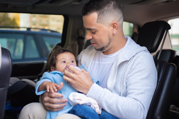 A Man Feeding His Child With A Bottle Of Milk