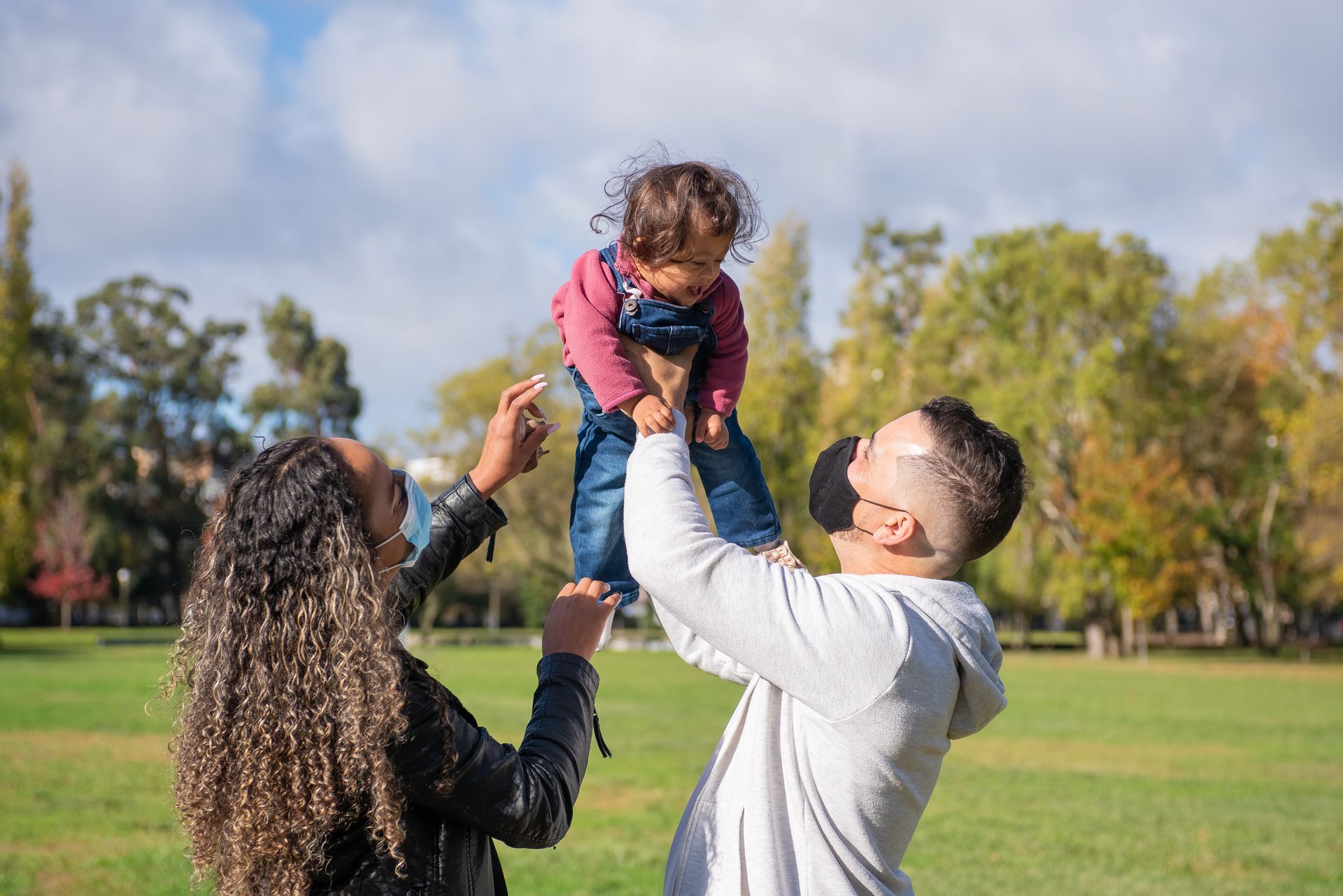 Family bonding outdoors in a park, wearing face masks for safety.