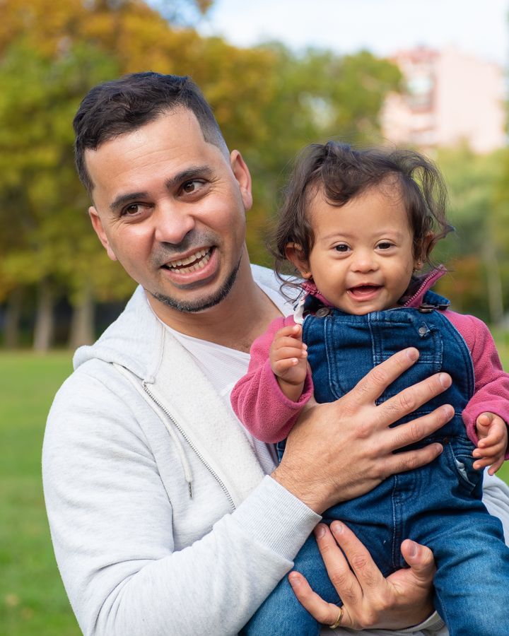 Father carrying his happy child with Down syndrome outdoors in a park