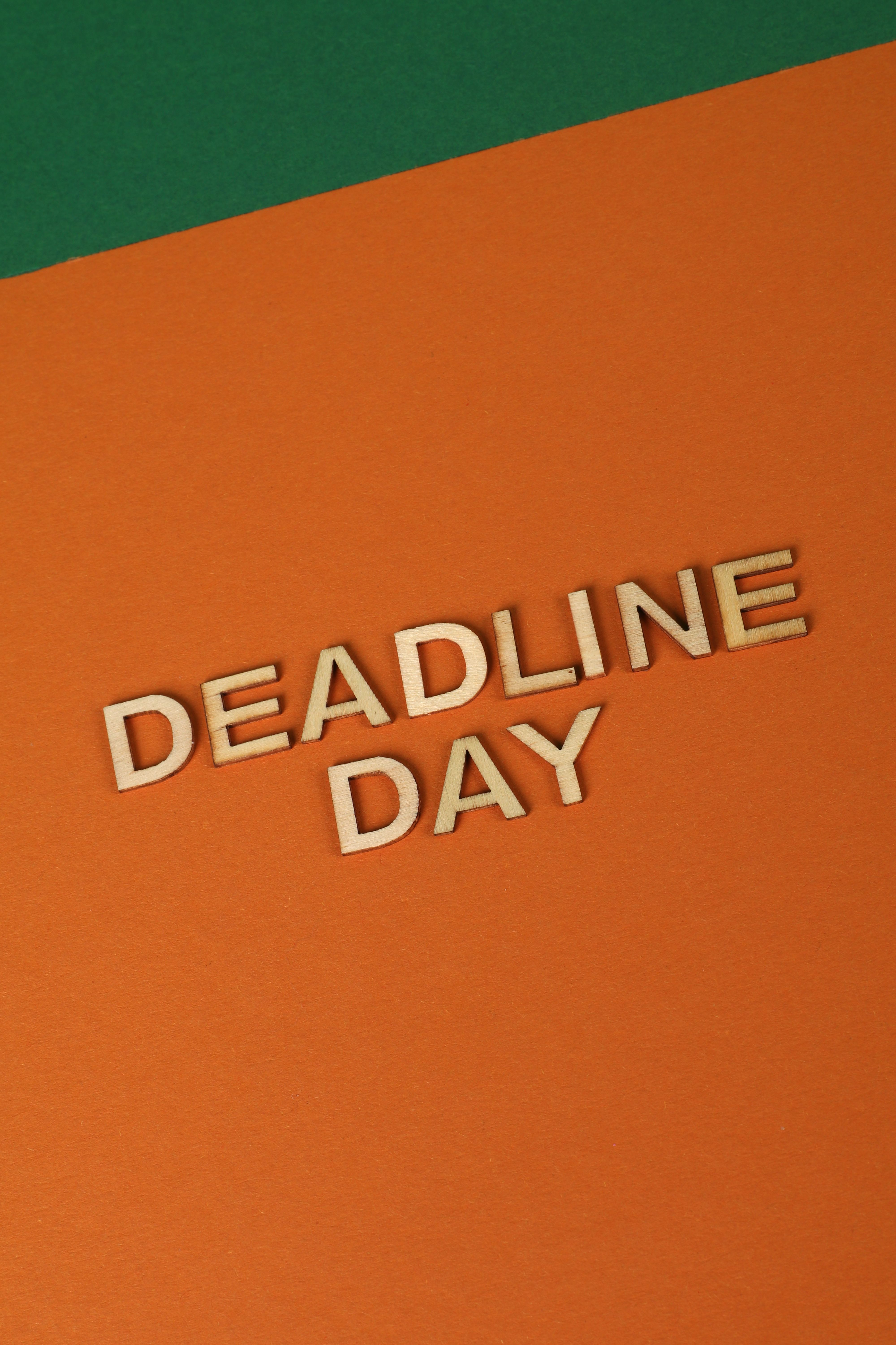 Vertical shot of 'Deadline Day' in wooden letters on an orange paper background.