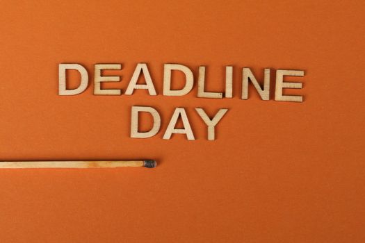 Conceptual image of a deadline with wooden letters and burnt matchstick on orange background.