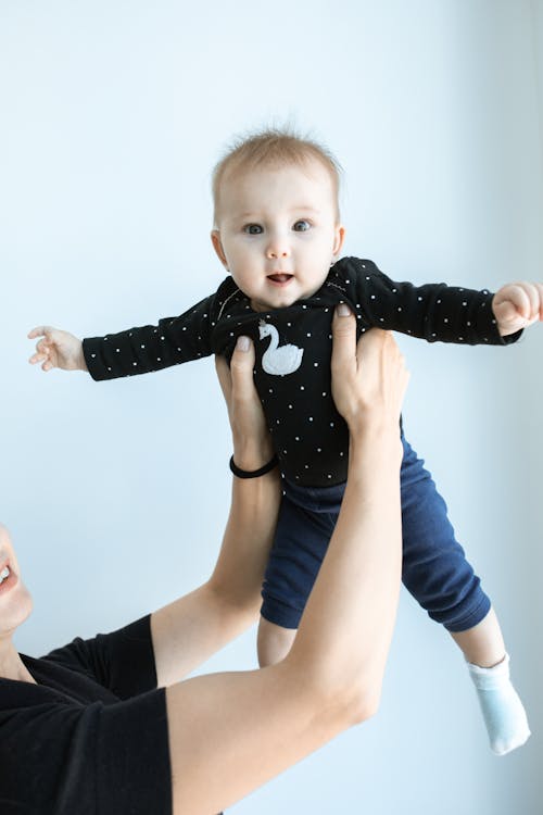 Wanita Berkemeja Biru Lengan Panjang Menggendong Bayi Dengan Onesie Polka Dot Hitam Putih