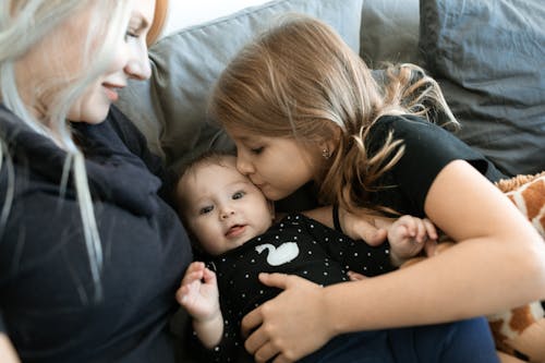 Little Girl in Black Shirt Kissing the Baby Beside their Mother