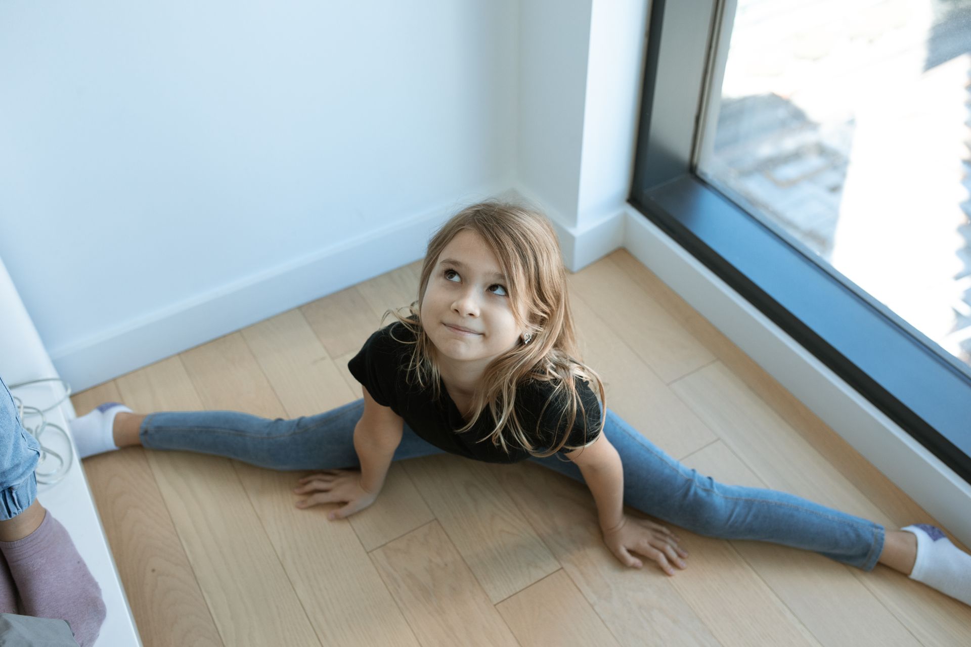 Young girl performing a split on wooden floor, showcasing flexibility and concentration indoors.