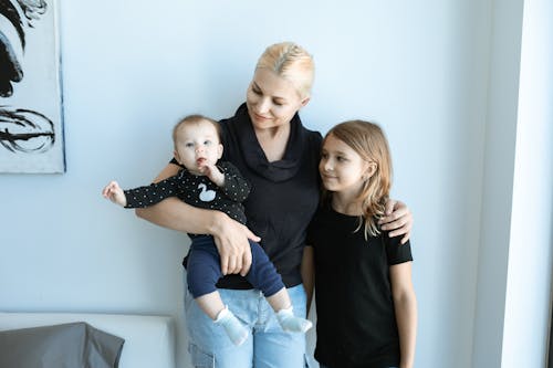 A Mother in Black Shirt Carrying the Baby while Standing Beside Her Daughter