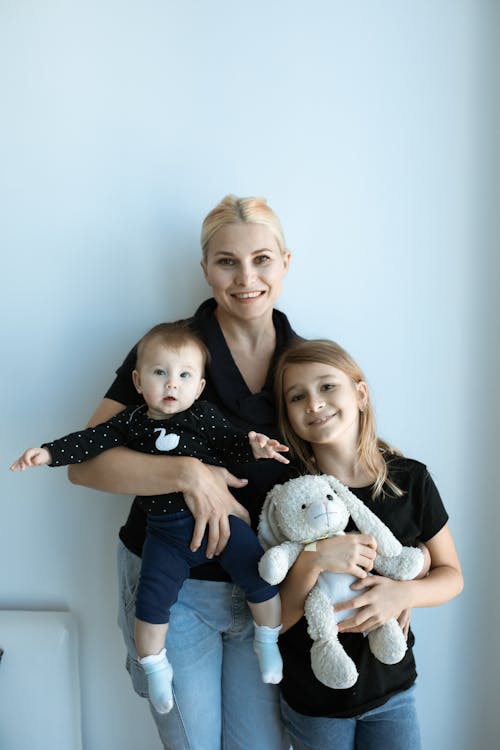 A Mother in Black Shirt Carrying a Baby Beside a Girl While Smiling at the Camera