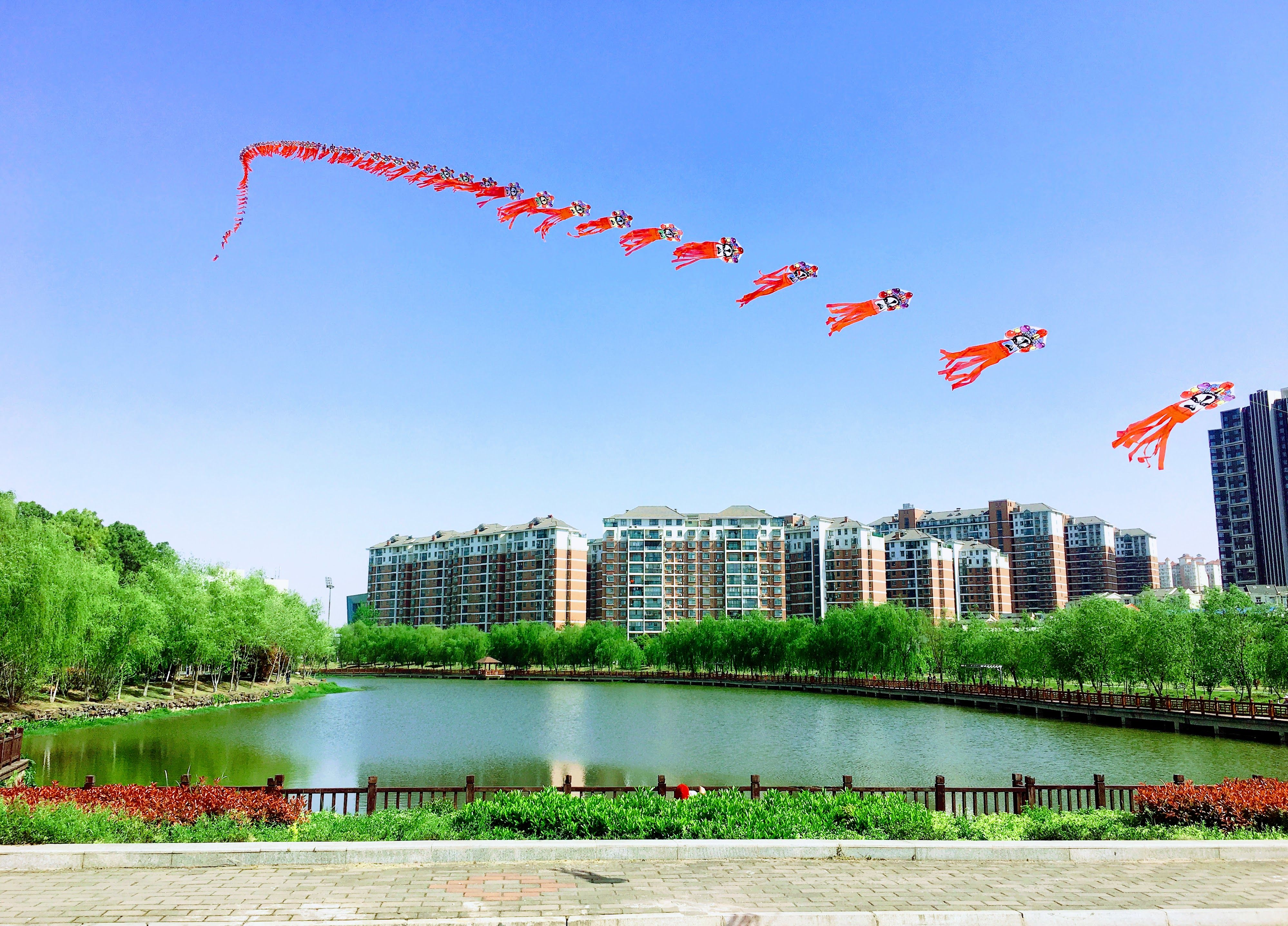 Vibrant kites soar above a lake and cityscape in Wuhan, China, showcasing urban nature.