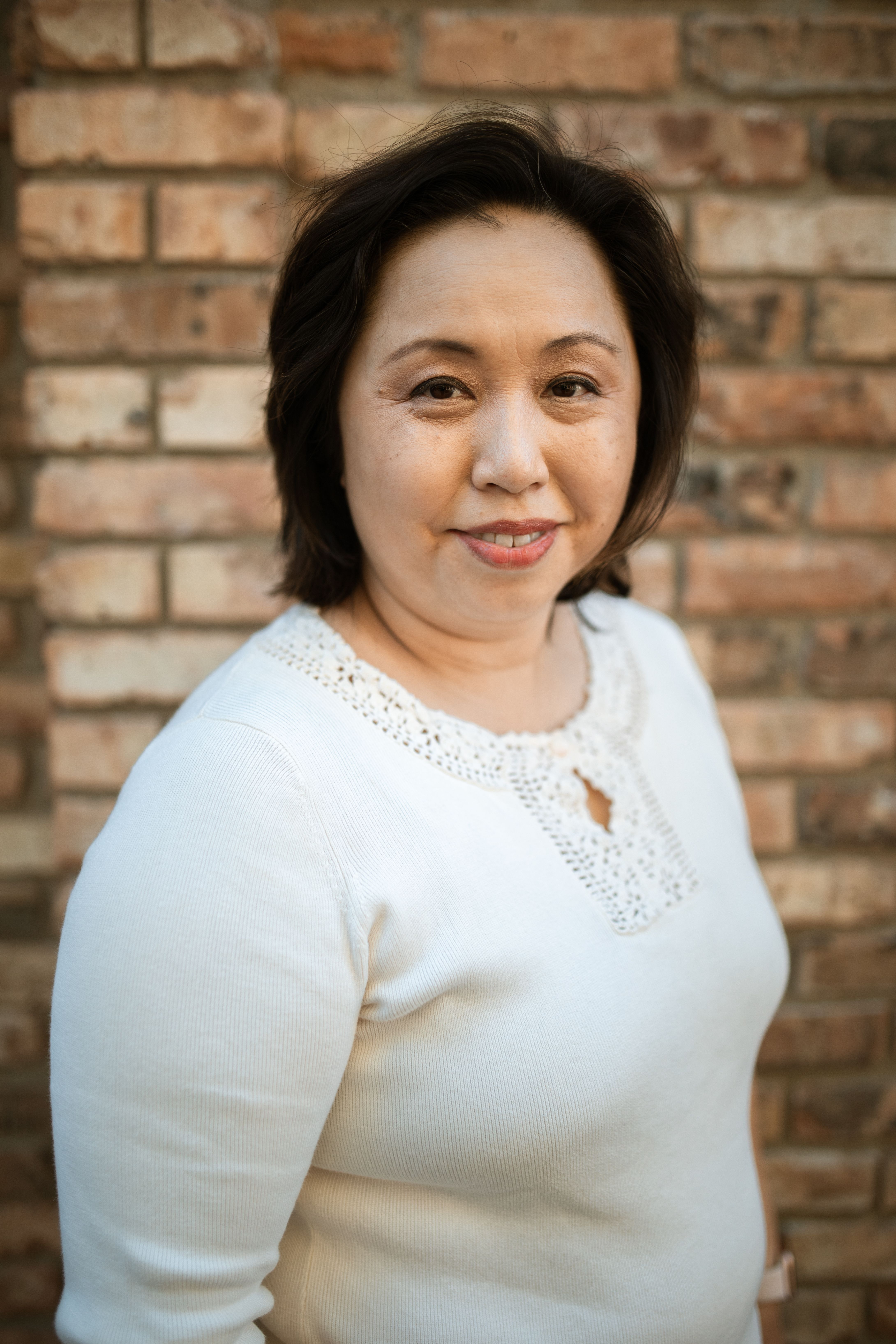 Portrait of a smiling woman in a white sweater posing against a brick wall.