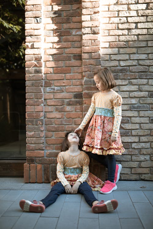 Two Girls in Printed Long Sleeve Dresses Beside the Brick Wall 