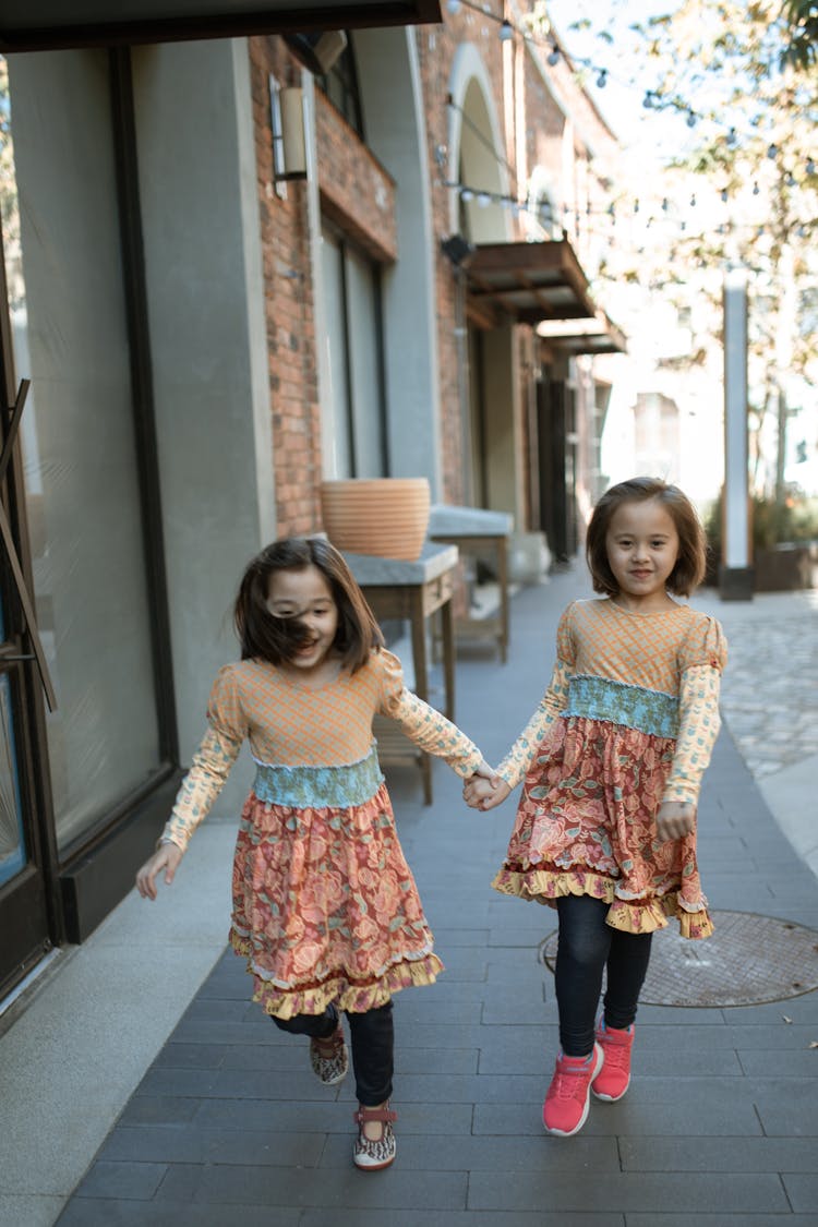 Two Girls Walking On Sidewalk Holding Hands