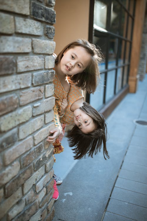 Free Girls Hiding Behind the Brick Wall while Looking Afar Stock Photo