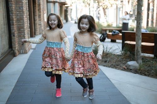 灰色のコンクリートの床に立っている白とピンクの花柄のドレスの2人の女の子