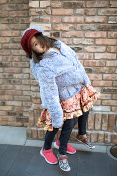 Charming young girl posing in colorful winter wear against a brick backdrop.