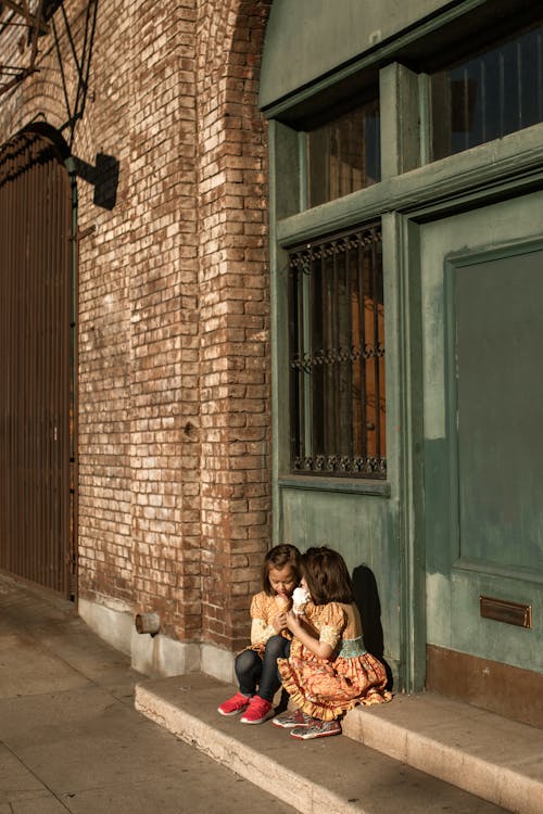 Two Girls Sitting on Concrete Steps Eating Ice Cream  
