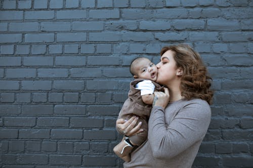 Woman in Brown Long Sleeve Shirt Kissing a Baby 