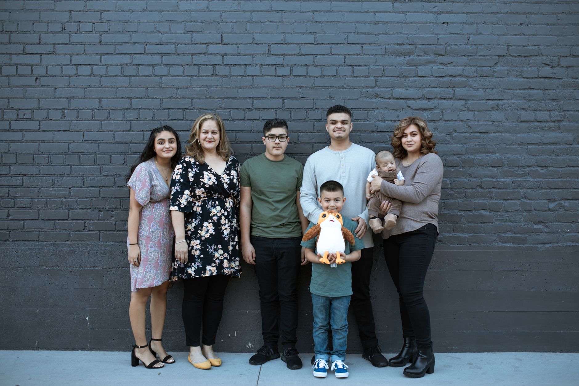 A joyful multigenerational family posing in front of a gray brick wall, symbolizing unity and togetherness.