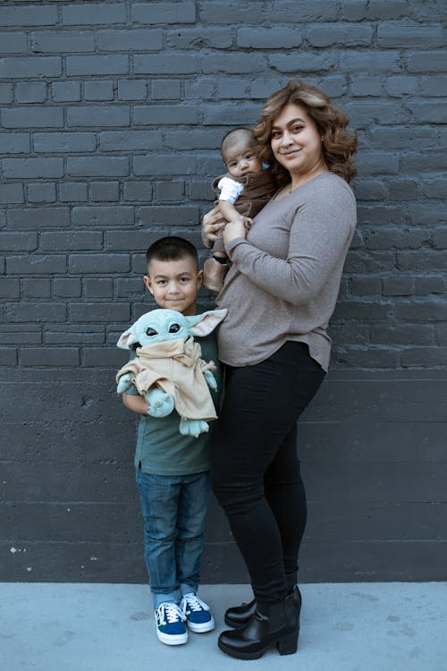 Woman in Brown Long Sleeve Shirt Standing Beside the Wall with Her Sons