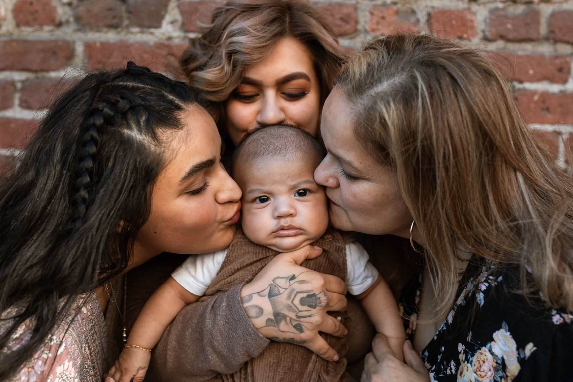 A family kiss surrounding a cute baby against a rustic brick wall.