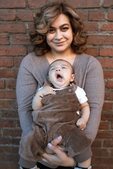 A joyful mother holding her yawning baby against a brick wall, showcasing warmth and family bonding.