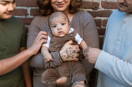 бесплатная Женщина в коричневом свитере с младенцем в белом комбинезоне Стоковое фото