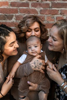 A loving family gathers around a baby for a joyful portrait against a brick wall.