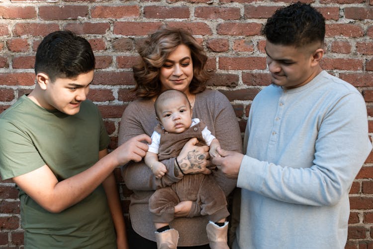 A Woman Carrying Her Baby Boy While Standing Between The Father And His Son