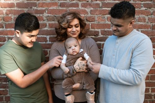 Free A joyful family holding a baby outdoors against a brick wall, highlighting love and unity. Stock Photo
