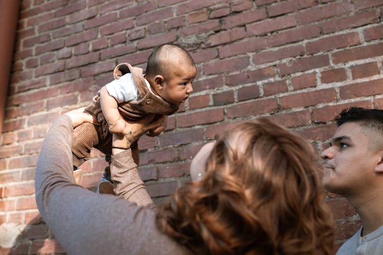 A Mother Lifting Her Baby Boy Near The Brick Wall