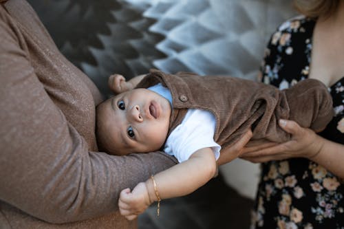 Free A Baby Boy in Brown Jumper Lying Down on Two Persons Hands Stock Photo