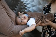 A Baby Boy in Brown Jumper Lying Down on Two Persons Hands