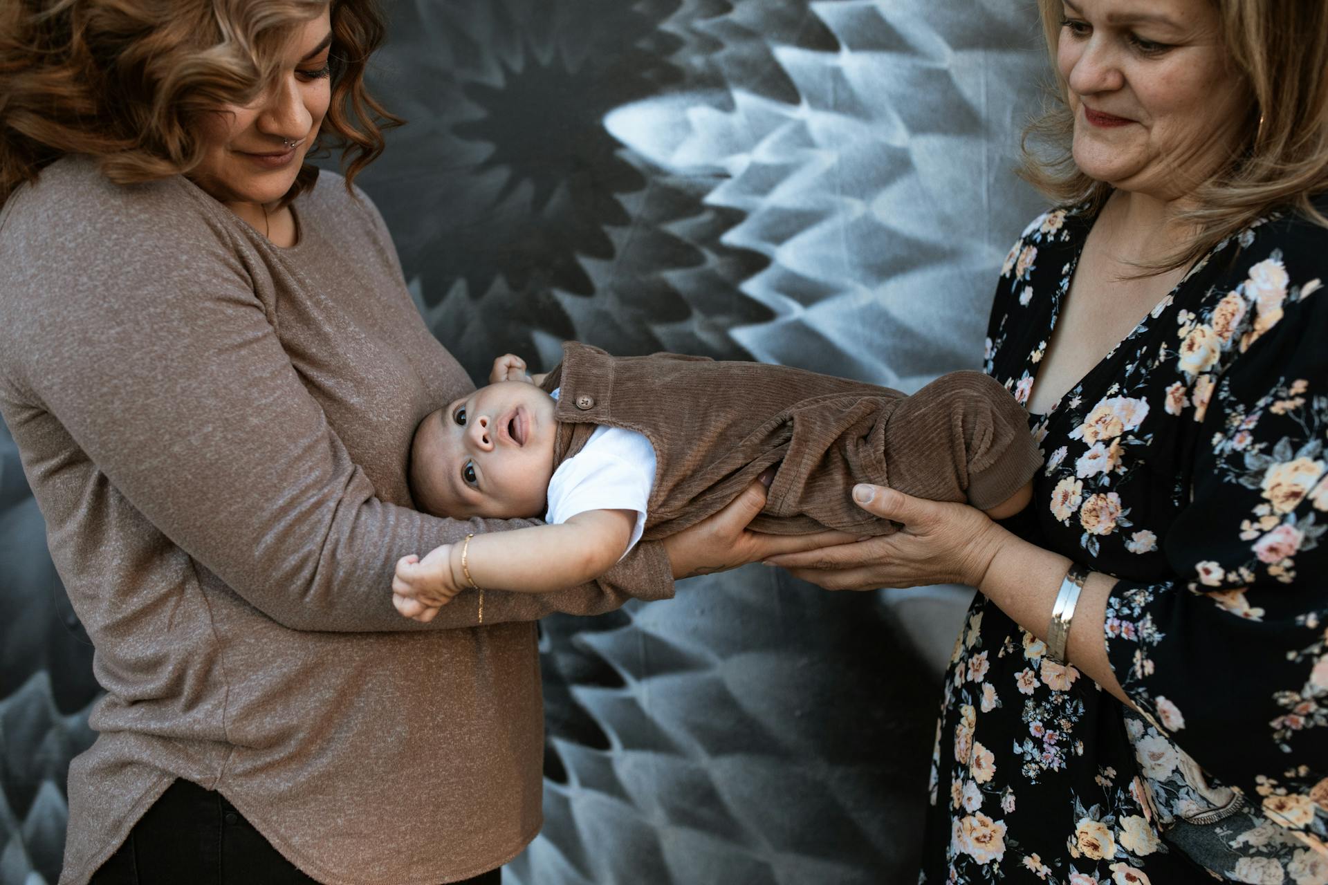 Two mothers lovingly hold a baby, showcasing warmth and togetherness in a family setting.