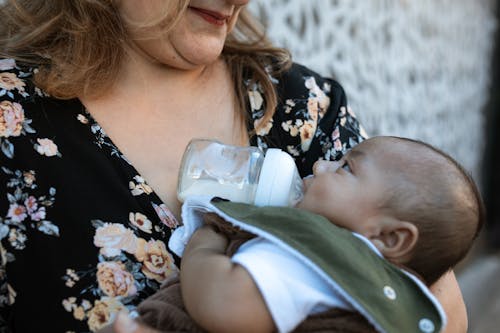 Free A Woman in Floral Shirt Carrying a Baby while Drinking Milk Stock Photo