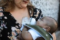 A Woman in Floral Shirt Carrying a Baby while Drinking Milk