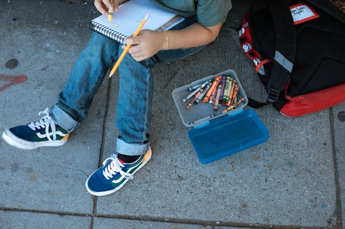 Free Child in Blue Denim Jeans and Colorful Sneakers Sitting on Floor Coloring on Sketchpad Stock Photo