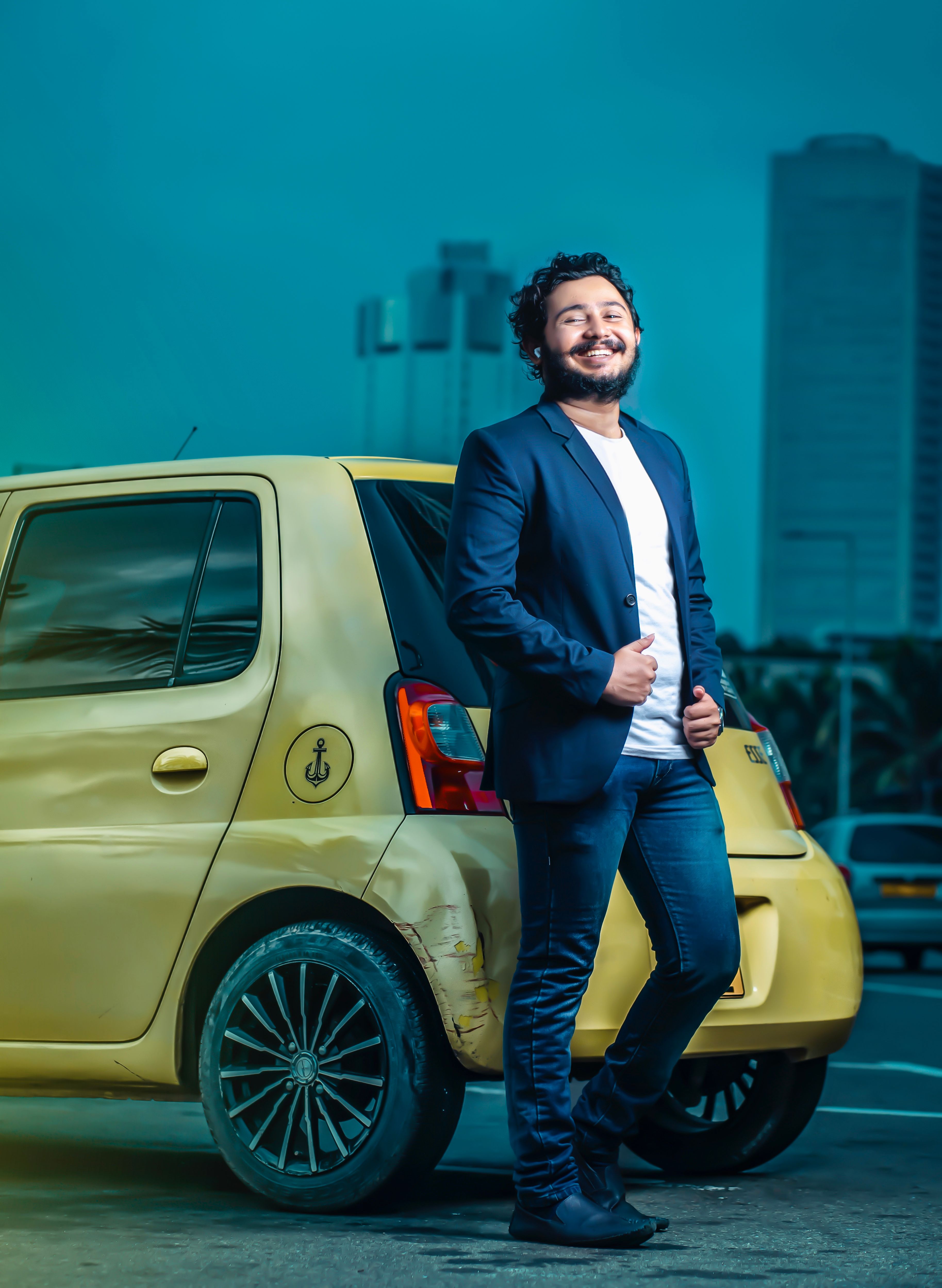 Happy man in blazer standing next to a yellow car in Sri Lanka's urban setting.