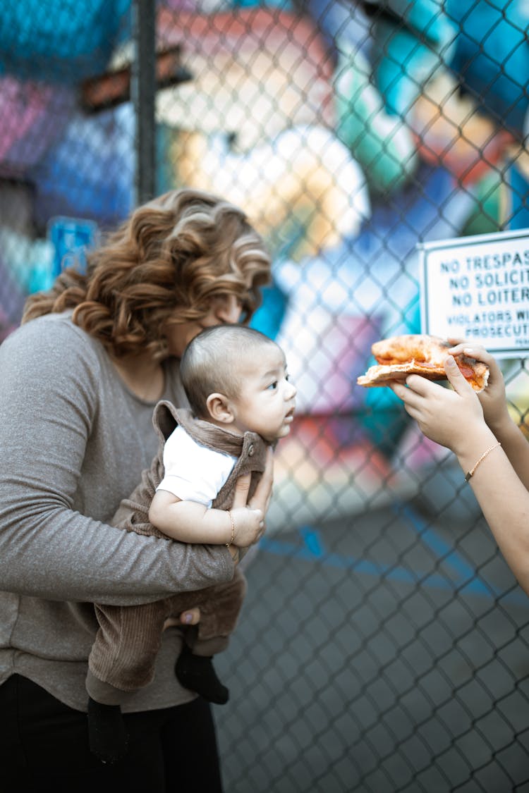 Woman In Gray Long Sleeve Shirt Carrying A Baby Boy Wearing A Brown Jumper