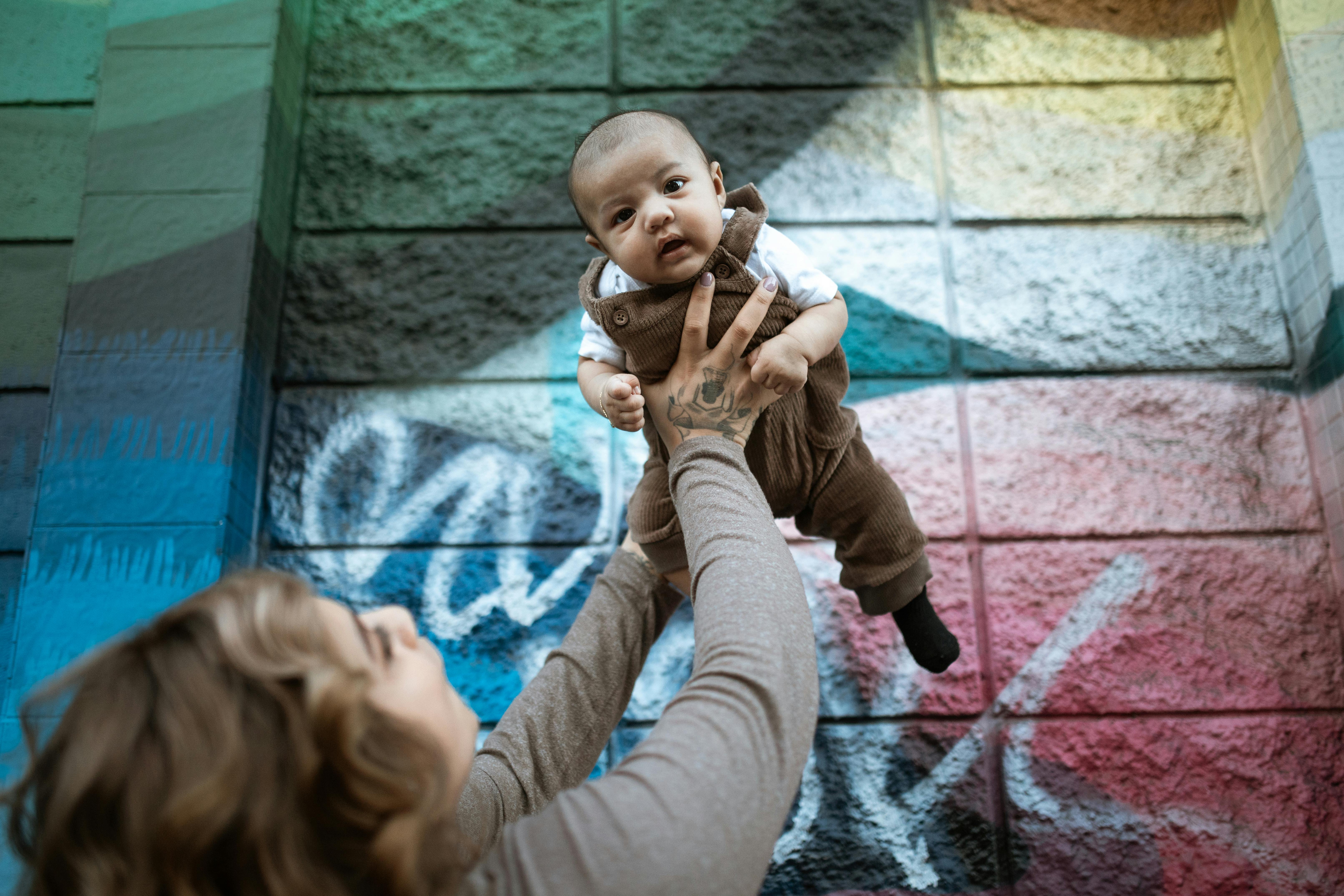 woman in pink long sleeve shirt carrying baby in brown and white long sleeve shirt