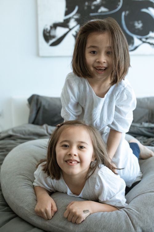 Free Two young siblings playfully smiling together on a comfortable bed indoors, exuding warmth and happiness. Stock Photo
