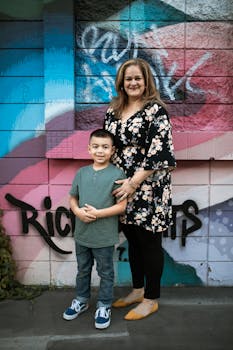 A cheerful mother and son pose by a vibrant graffiti wall, exuding happiness and family bond.