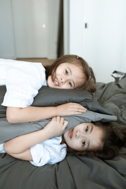 Two Girls Lying on Bed Hugging a Gray Pillow