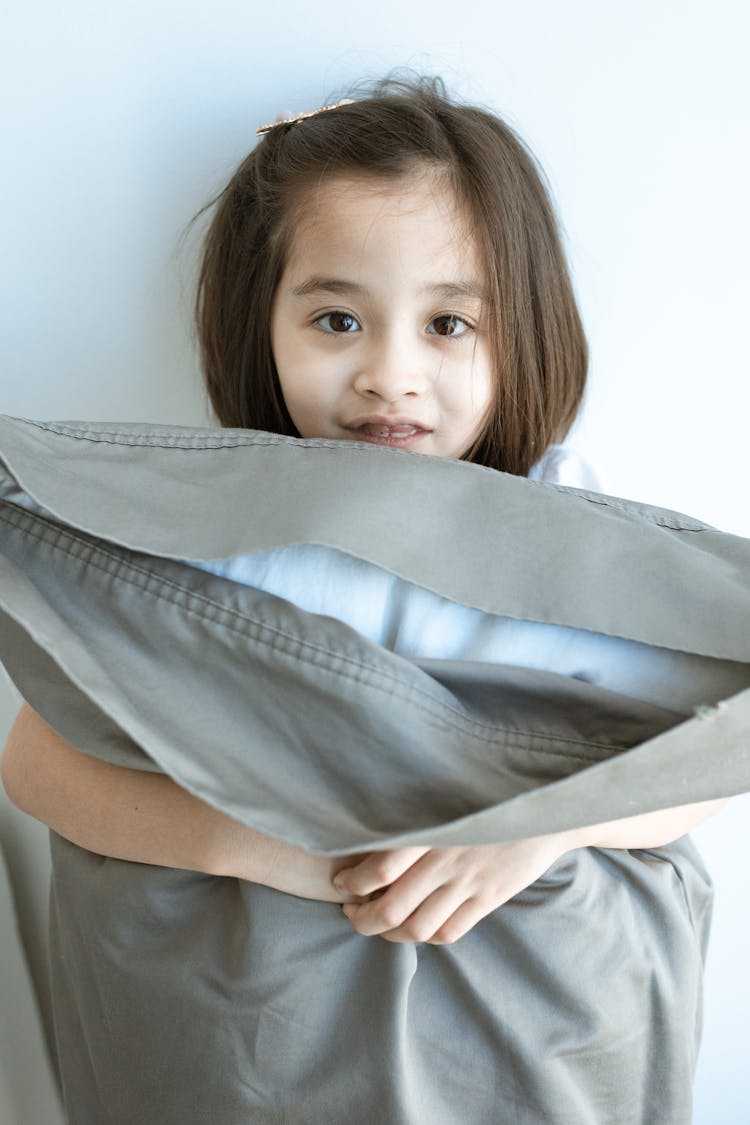 A Cute Girl Standing Hugging A Gray Pillow