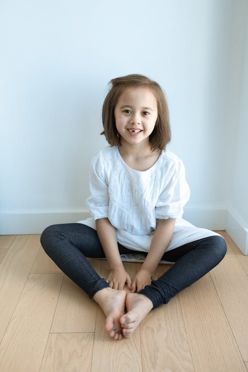 Menina Com Camiseta Branca Com Gola Redonda E Jeans Azul, Sentada No Chão De Madeira Marrom