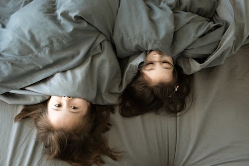 Two Children Covering Mouths With Blanket While Lying Down