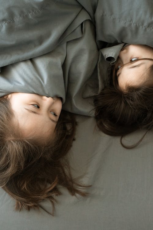 Free Two Girls Lying Down on Bed Covering Mouth With Blanket Stock Photo