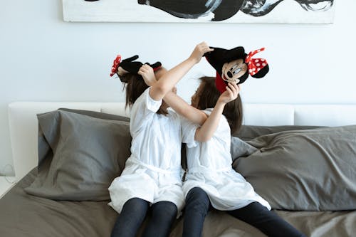 Two Girls Playing Together While Sitting on Bed