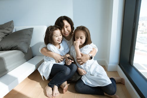 Free Parent Hugging Her Kids While Sitting on the Wooden Floor Stock Photo