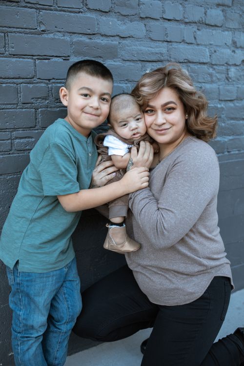 Free Heartwarming family portrait featuring a mother hugging her two sons against a brick wall. Stock Photo