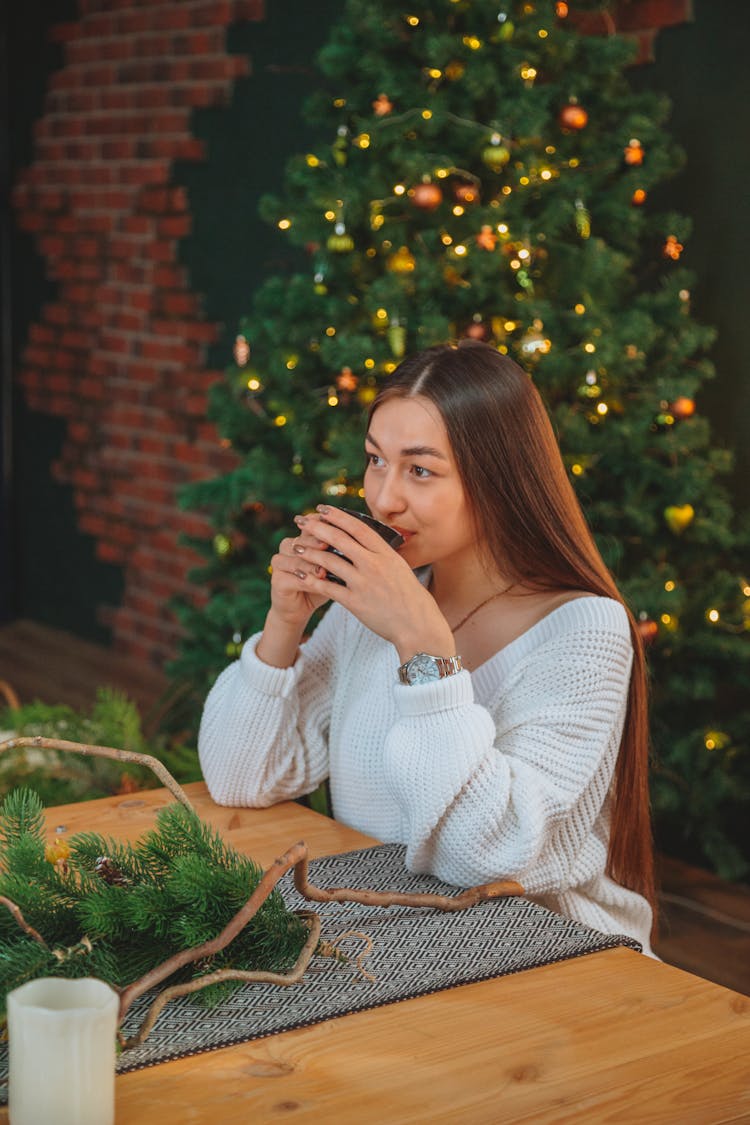 Dreamy Woman Drinking Tea Against Christmas Tree